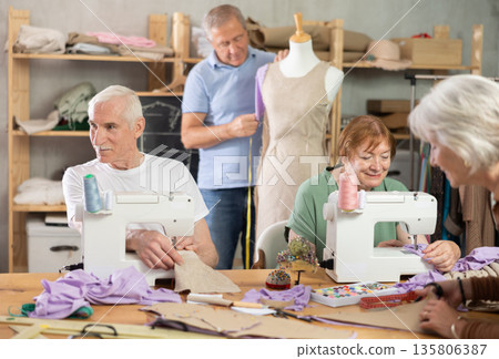 Man and woman stitching at machines during group sewing class Man and woman stitching at machines during group sewing class 135806387