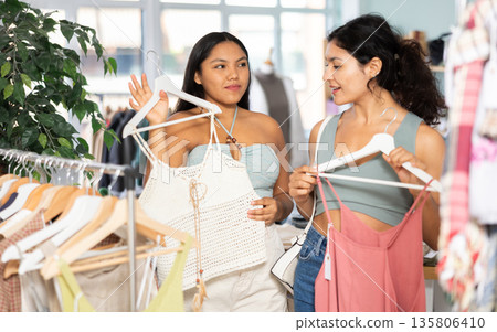 Two girlfriends chooses dresses or o tops for the summer period in fashionable clothing store Two girlfriends chooses dresses or o tops for the summer period in fashionable clothing store 135806410