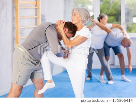 Senior woman in pair with middle-aged coach train Krav Maga and self-defense skills. 135806414