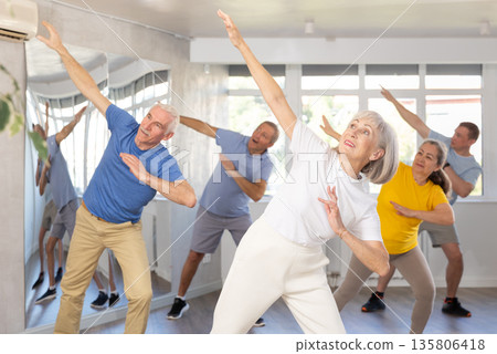 Elderly woman practicing Tai Chi with group in training room 135806418