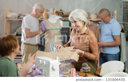 Some people discuss pattern, while others sew using sewing machine, work with mannequin Some people discuss pattern, while others sew using sewing machine, work with mannequin 135806430