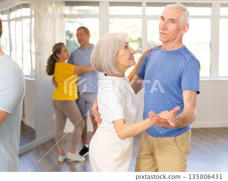 Group of elderly pensioners learn to dance a couple tango dance in dance class 135806431