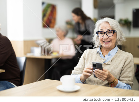 Elderly woman holding mobile phone in coffee shop 135806433