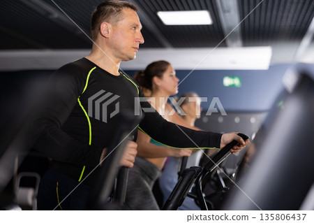 Strong sportsman training at elliptical machine in gym 135806437