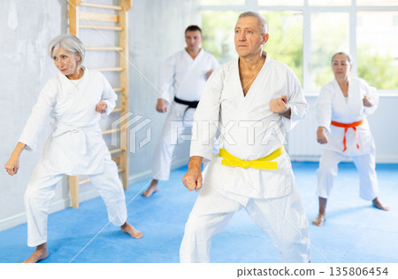 Old man attendee of karate classes practicing kata standing in row with others Old man attendee of karate classes practicing kata standing in row with others 135806454