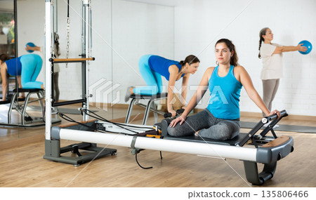 Young woman practicing pilates on reformer tower equipment in sports hall Young woman practicing pilates on reformer tower equipment in sports hall 135806466