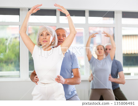 Senior ballet couple partners preparing in rehearsal for contest, training demi plie ballet poses with support in classroom Senior ballet couple partners preparing in rehearsal for contest, training demi plie ballet poses with support in classroom 135806491