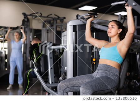 Athletic woman is engaged in simulator - develops biceps and triceps Athletic woman is engaged in simulator - develops biceps and triceps 135806510