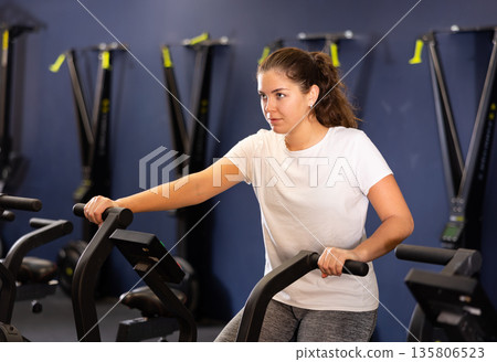 Young girl cycling on stationary bike during training in gym 135806523
