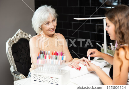 Unrecognizable girl manicure master files nails and performs grooming procedure for senior woman Unrecognizable girl manicure master files nails and performs grooming procedure for senior woman 135806524