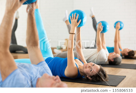 Middle-aged woman practicing pilates with ball in gym area 135806533