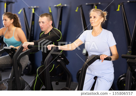 Focused mature woman using elliptical machine in gym 135806557