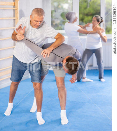 Self defense lesson - elderly man twists the arm of attacking man with painful hold in gym Self defense lesson - elderly man twists the arm of attacking man with painful hold in gym 135806564