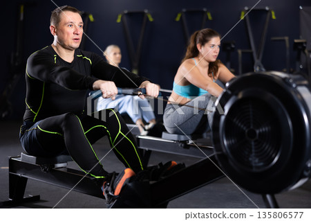 Motivated adult man working out on rowing machine in gym Motivated adult man working out on rowing machine in gym 135806577