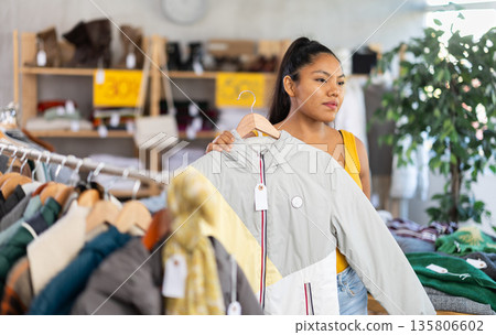 Happy young girl choosing down jacket in clothing store Happy young girl choosing down jacket in clothing store 135806602