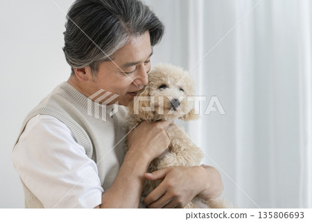 一位五十多歲的男子抱著他心愛的狗狗(一隻十個月大的比熊貴賓犬)-展現與狗狗相伴的生活。 一位五十多歲的男子抱著他心愛的狗狗(一隻十個月大的比熊貴賓犬)-展現與狗狗相伴的生活。 135806693