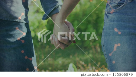 Holding couple in denim clothing interlocking hands in sunny garden, green foliage theme 135806879
