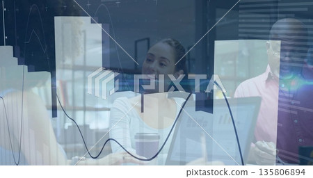 Central female coworker reviewing data graphs on laptop in office meeting room, with coffee cup 135806894