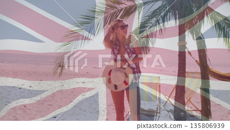 Standing in checkered shirt, shorts on sandy beach, with straw hat, palm tree, Union Jack flag Standing in checkered shirt, shorts on sandy beach, with straw hat, palm tree, Union Jack flag 135806939