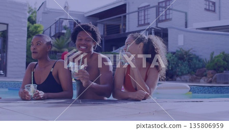 Leaning three friends in swimwear sipping drinks with straws at backyard pool, with pool float 135806959