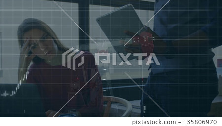 Female coworker reviewing tablet with male colleague at office desk, open laptop mug visualization 135806970