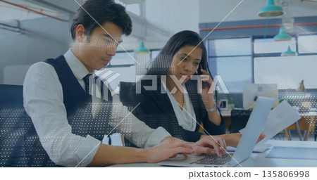 Office colleagues in suits typing and speaking at white desk with laptop, documents, smartphone 135806998