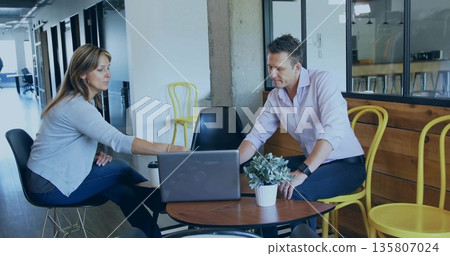 Colleagues casually dressed talking at office lounge, with open laptop, coffee cup and potted plant Colleagues casually dressed talking at office lounge, with open laptop, coffee cup and potted plant 135807024
