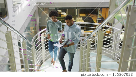 Reviewing colleagues examining clipboard, smartphone on mezzanine staircase, security briefing Reviewing colleagues examining clipboard, smartphone on mezzanine staircase, security briefing 135807038