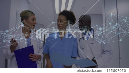 Walking team in lab coats discussing files in hospital corridor with smartphone under overlay Walking team in lab coats discussing files in hospital corridor with smartphone under overlay 135807050