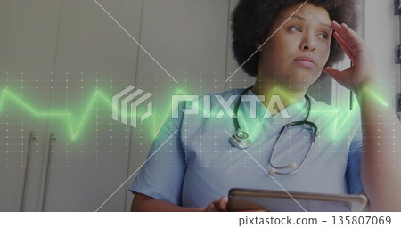 Standing nurse wearing blue scrubs, stethoscope, holding tablet in office, ECG overlay, copy space Standing nurse wearing blue scrubs, stethoscope, holding tablet in office, ECG overlay, copy space 135807069