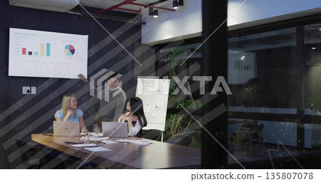 Pointing presenter guiding colleagues observing online sales tracker on screen in boardroom 135807078