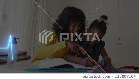 Leaning mother in yellow top pointing at workbook while daughter writing at study nook, with pencil 135807104
