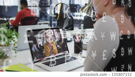 Sitting Asian woman looking at call on laptop in office with currency overlay, copy space 135807152