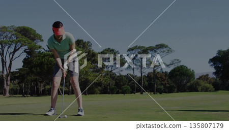 Leaning woman wearing pink visor aligning putter behind golf ball on putting green with trees Leaning woman wearing pink visor aligning putter behind golf ball on putting green with trees 135807179