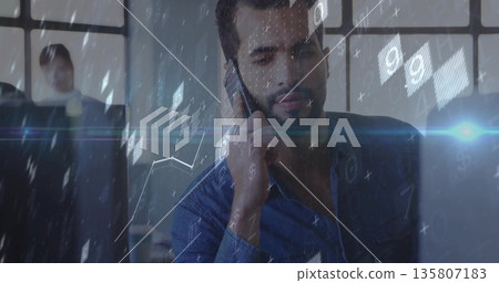 Bearded man in blue shirt speaking on smartphone at office desk, with laptop, data overlays Bearded man in blue shirt speaking on smartphone at office desk, with laptop, data overlays 135807183
