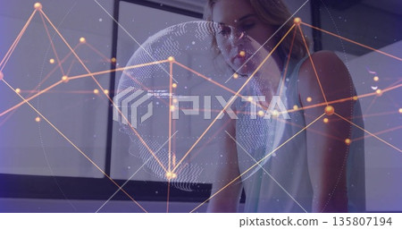 Leaning woman wearing sleeveless top focusing on computer screen at desk with tech network overlay 135807194