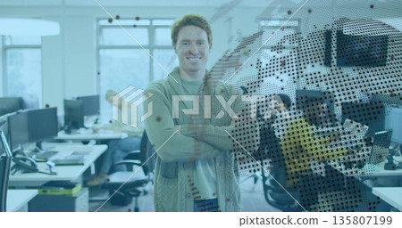 Standing man in cardigan sweater crossing arms and smiling at open office with dot-matrix overlay Standing man in cardigan sweater crossing arms and smiling at open office with dot-matrix overlay 135807199