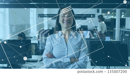 Standing confident mid adult female crossing arms in modern office, with monitors, network overlay 135807200