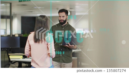 Discussing financial data professional holding laptop in office floor with currency symbols overlay 135807274