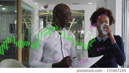 Standing in business attire reviewing digital charts in office with pen printout and coffee cup 135807289