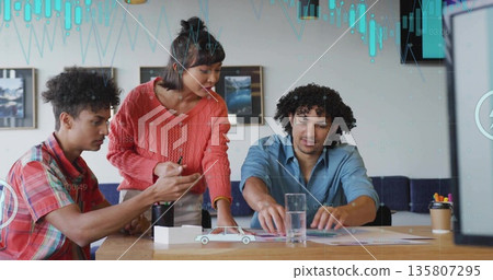 Reviewing colleagues at conference table examining charts, with woman in coral sweater holding pen Reviewing colleagues at conference table examining charts, with woman in coral sweater holding pen 135807295