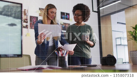Reviewing women colleagues examining printed sheets at creative office, with camera lens on table 135807318