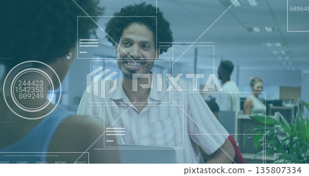 Smiling man leaning on desk talking at open-plan office with laptop, digital overlay graphics Smiling man leaning on desk talking at open-plan office with laptop, digital overlay graphics 135807334