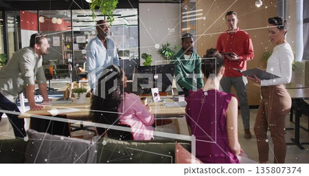Collaborating team of coworkers discussing strategy in open-plan office, with monitor and greenery 135807374