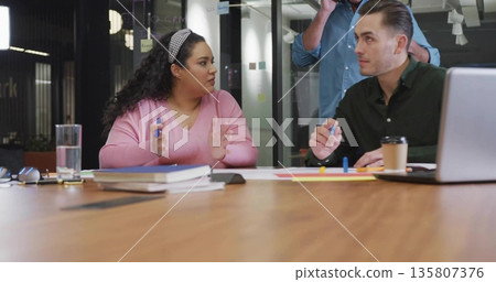 Brainstorming three professionals developing ideas in office meeting room, with markers and laptop Brainstorming three professionals developing ideas in office meeting room, with markers and laptop 135807376