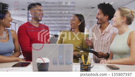 Discussing coworkers standing at desk in office, with laptop tablet smartphone coffee cup clipboard Discussing coworkers standing at desk in office, with laptop tablet smartphone coffee cup clipboard 135807397