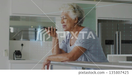 Leaning senior woman holding smartphone projecting holographic grid in kitchen, with metal railing Leaning senior woman holding smartphone projecting holographic grid in kitchen, with metal railing 135807425