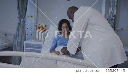 Examining doctor leaning over hospital bed, checking patient arm with blue gown and flowers Examining doctor leaning over hospital bed, checking patient arm with blue gown and flowers 135807445