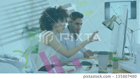 Woman in blouse and man in shirt analyzing charts on monitors at office with coffee cup 135807480