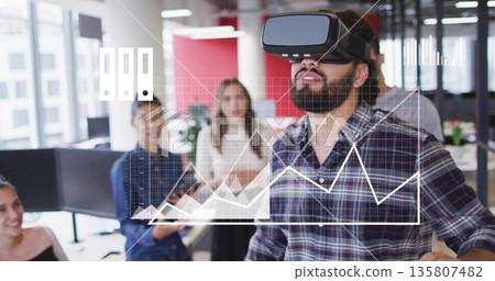 Testing VR simulation by casual man wearing headset at office desk, coworkers observing with tablet 135807482